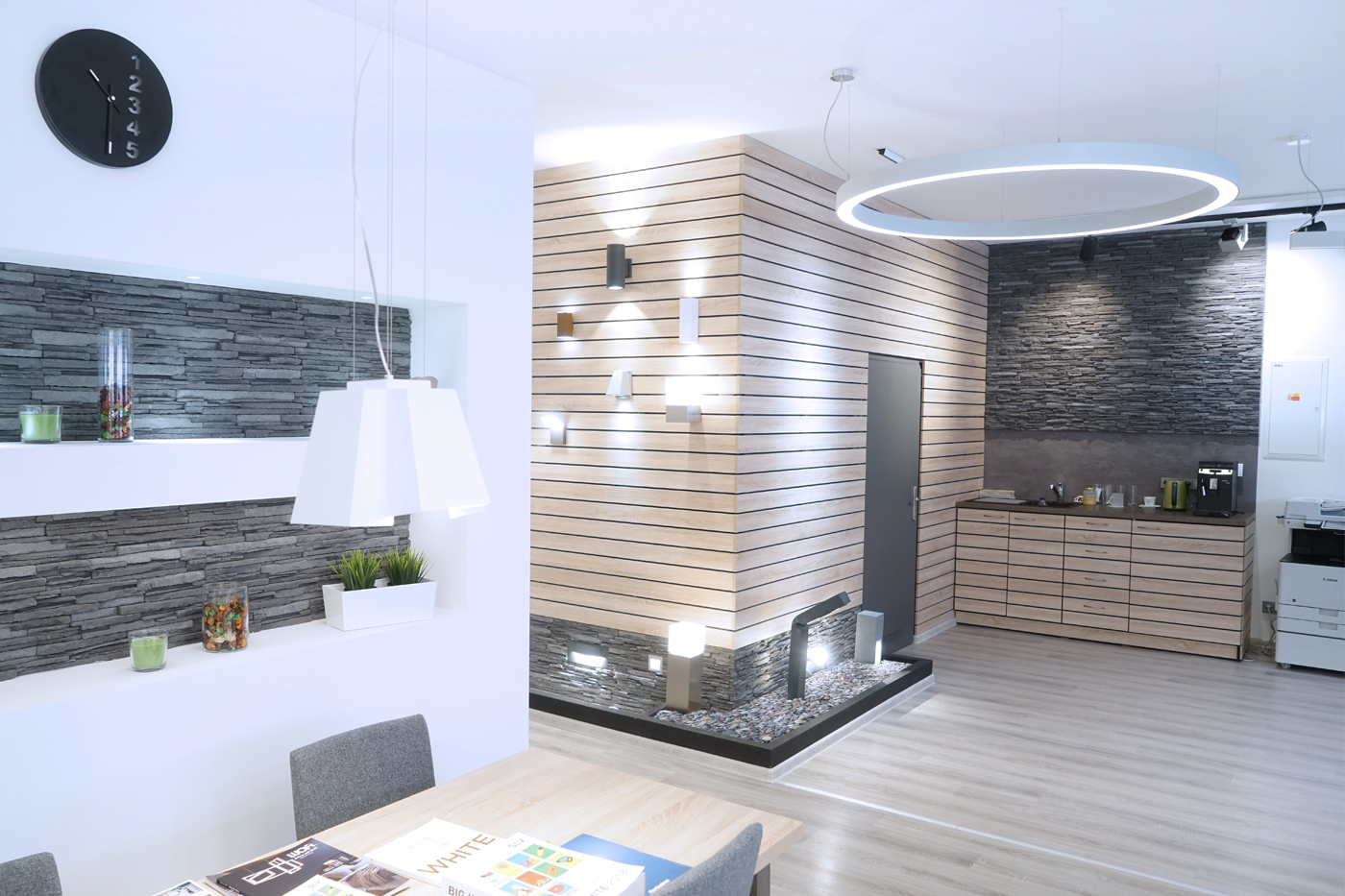 Venkovní a fasádní svítidla jsou prezentovány na zdi podobné moderní fasádě, která přechází do funkční kuchyňky.
